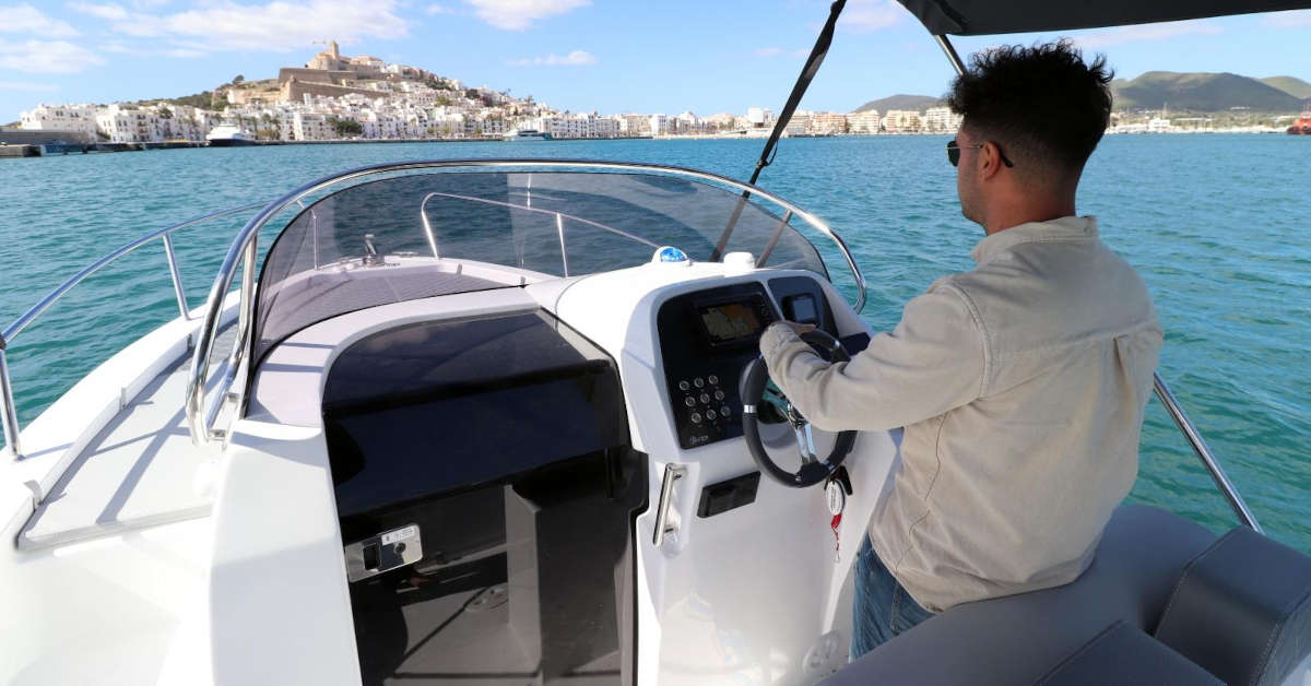 A man sailing in the port of Ibiza, with Dalt Vila in the background.